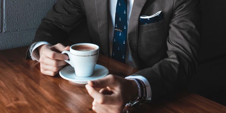 A man in a suit sitting at a table with a cup of coffee. - mybiked.com