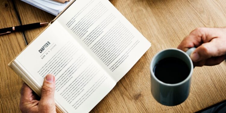 A man is reading a book while holding a cup of coffee. - mybiked.com