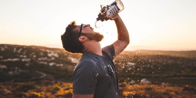 A man drinking water from a bottle at sunset. - mybiked.com